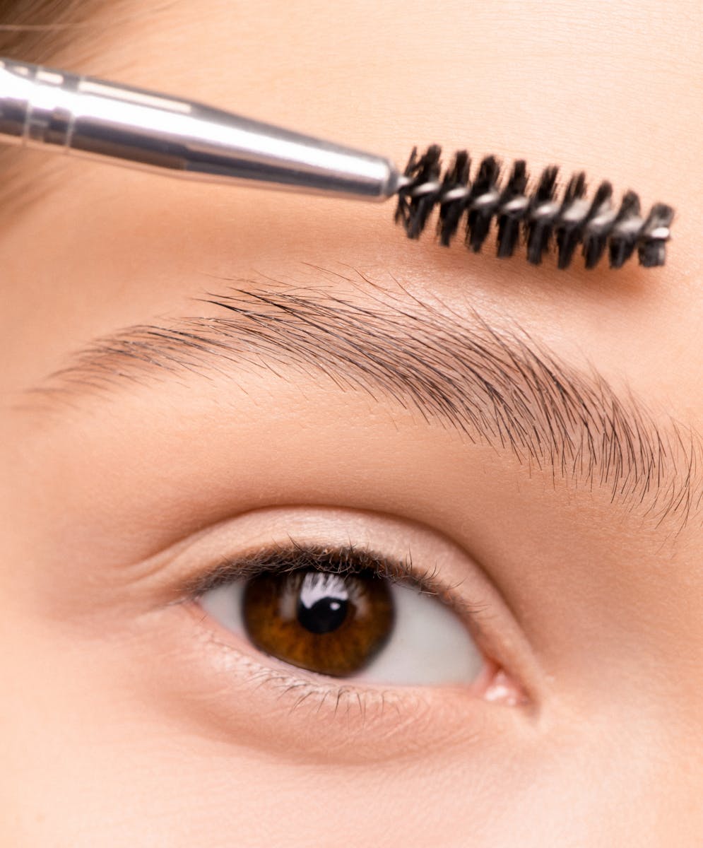 A detailed close-up photo of a woman's eyebrow being groomed with a brush.